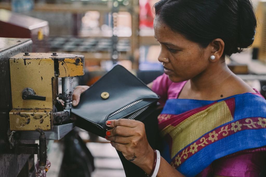Woman in a sari using a machine to add a snap to a black leather bag in a workshop