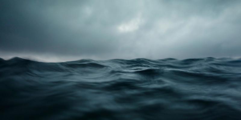 Choppy dark blue-grey ocean waves under a stormy overcast sky at water level