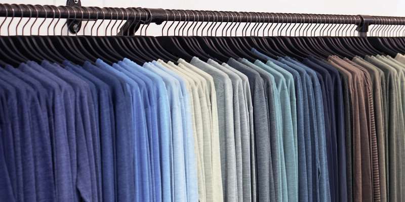 Rack of color-graded apparel on hangers, from blue to grey to tan, representing the fashion supply chain.