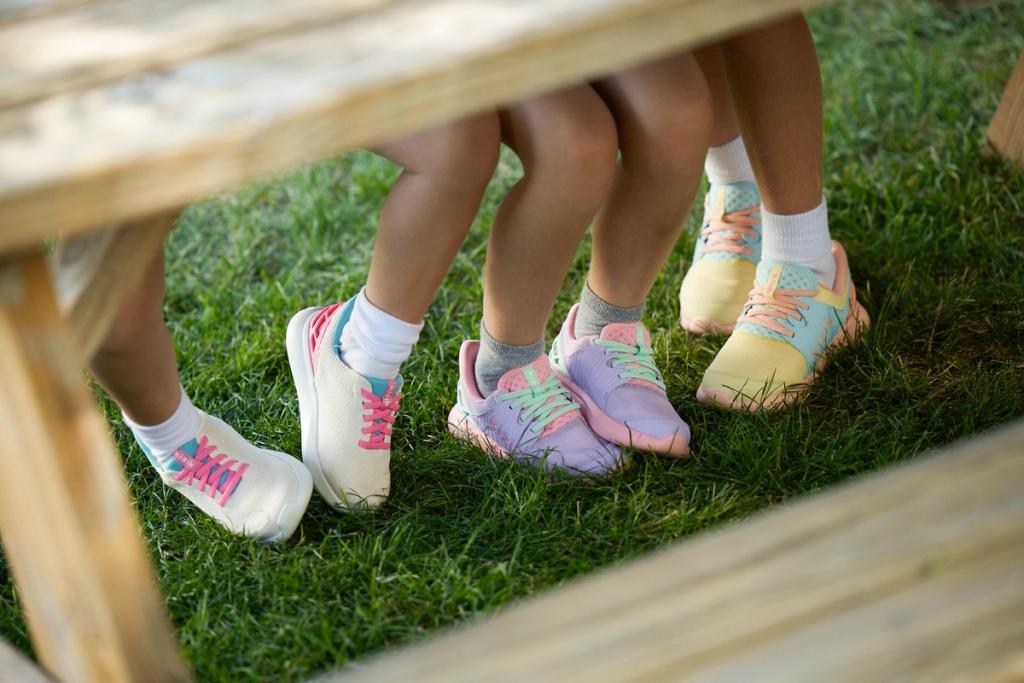 Children's legs in colorful pastel Kizik sneakers seen through a wooden bench on grass
