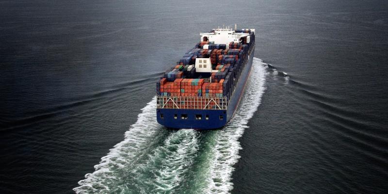 Container ship fully loaded with stacked cargo containers sailing on open ocean, viewed from astern.