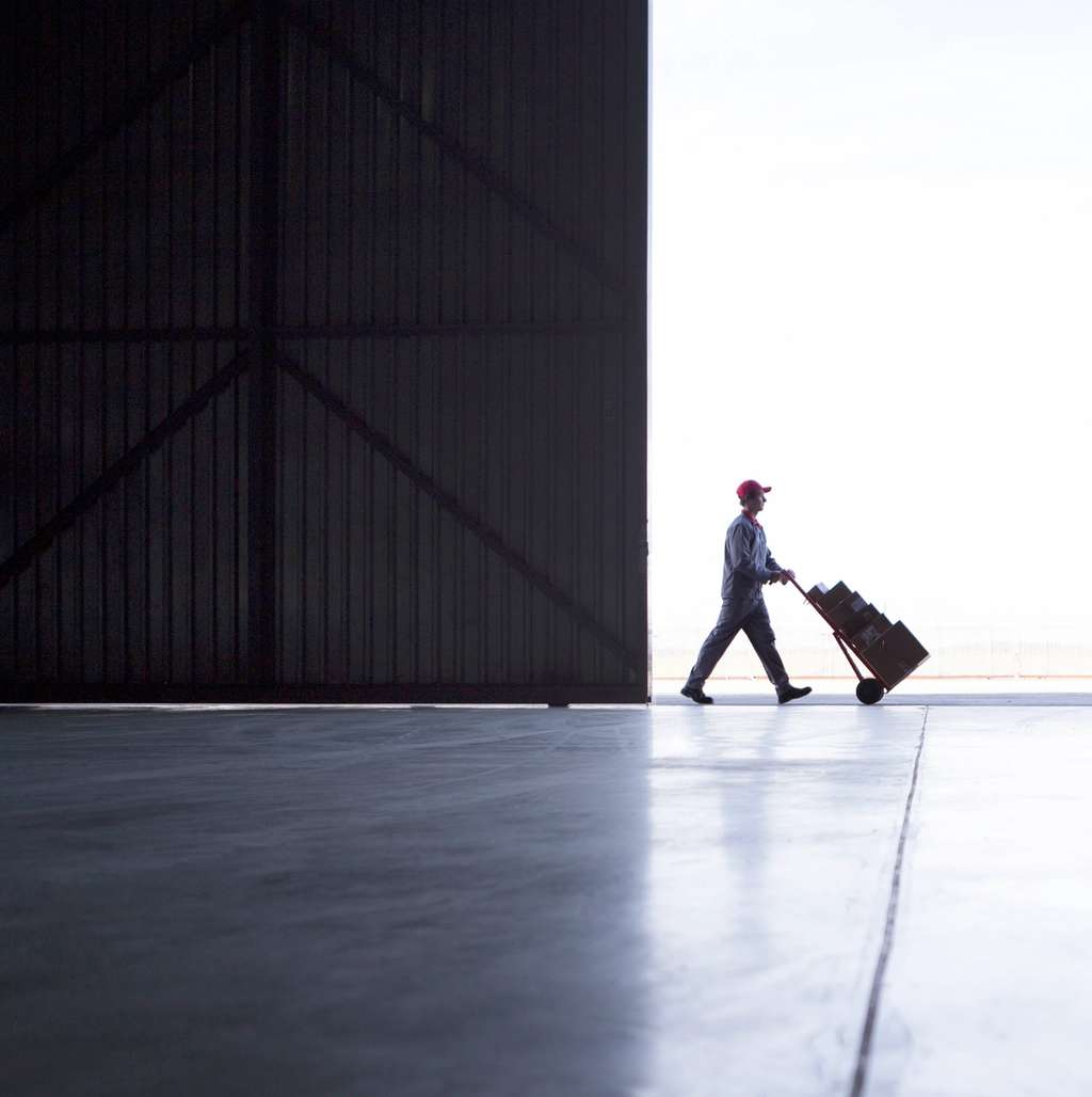 Female small business owner on the phone while working at a laptop, surrounded by shipping boxes in a warehouse office.