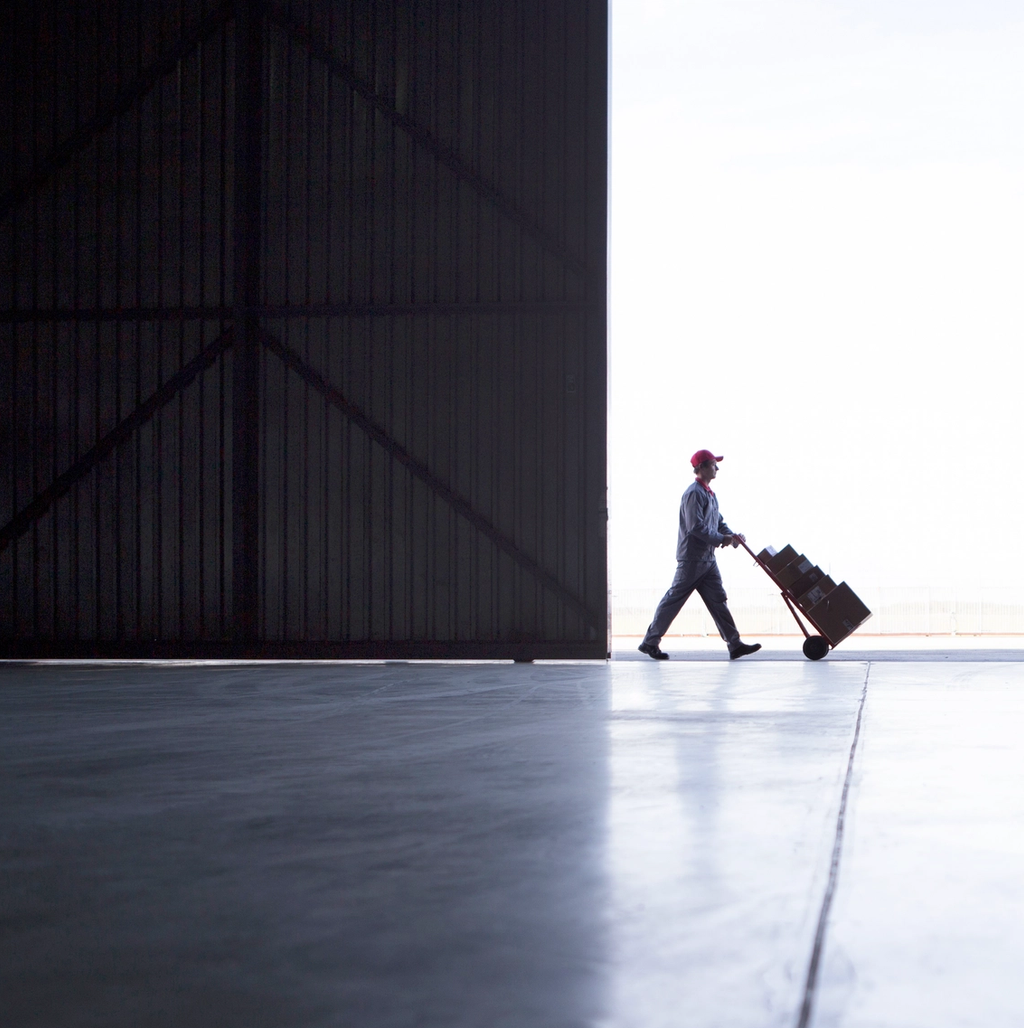 Female small business owner on the phone while working at a laptop, surrounded by shipping boxes in a warehouse office.