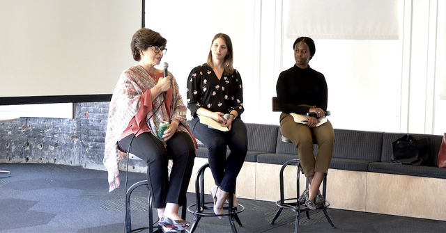 Three women seated on stools on a stage holding notes during a panel discussion