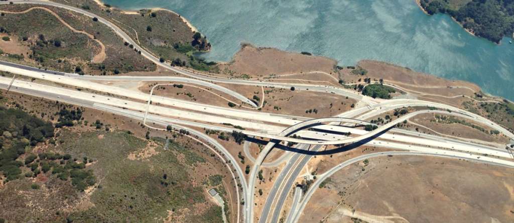 Aerial view of a multi-level highway interchange beside a reservoir