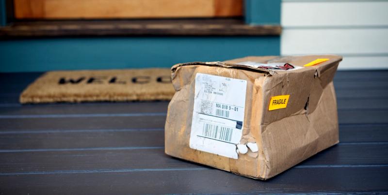 Crushed cardboard parcel marked FRAGILE on a porch beside a WELCOME doormat