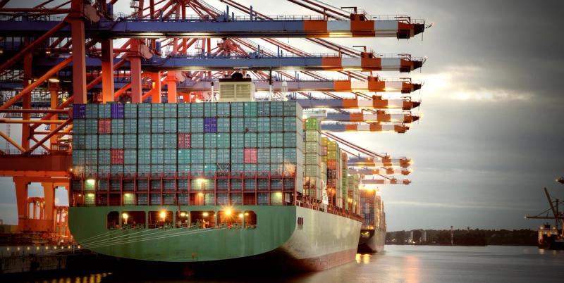 Loaded container ship docked at dusk beneath a row of orange gantry cranes