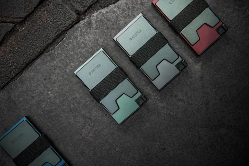 Four Ekster slim cardholder wallets in different colors arranged on dark stone