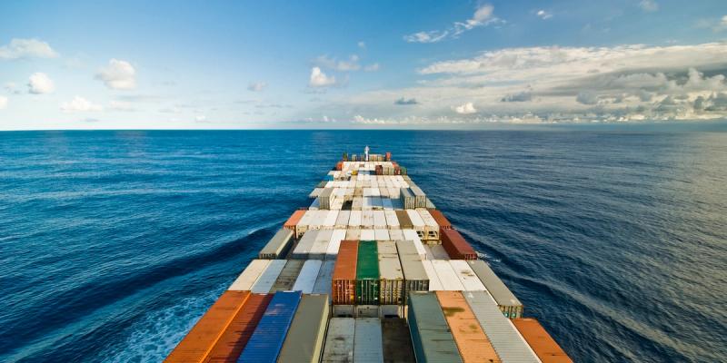 Container ship sailing on calm open ocean at sunset with mountains on the horizon