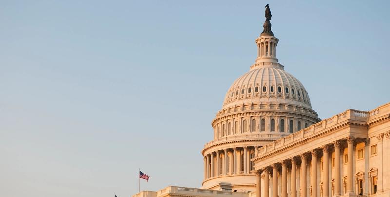 U.S. Capitol dome at golden hour with an American flag against a clear sky.