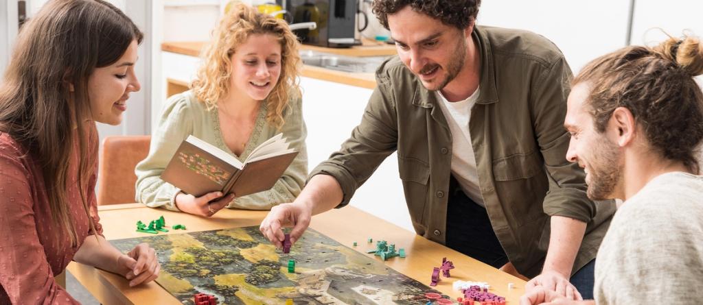 Four friends gathered around a kitchen table playing a colorful strategy board game