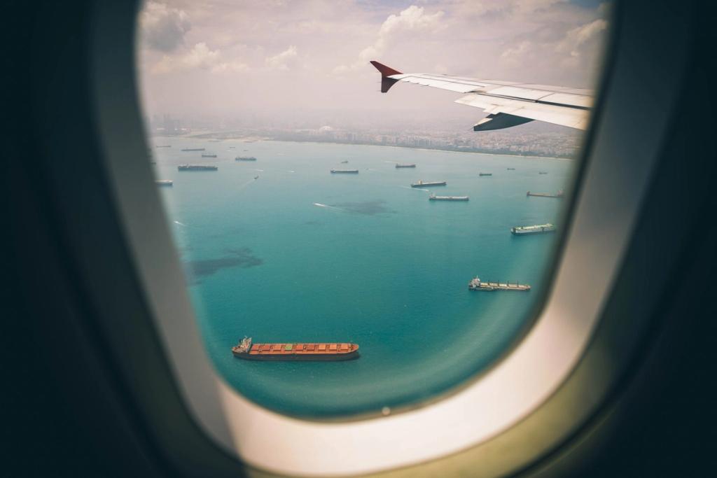 View through an airplane window of cargo ships anchored in turquoise water near a coastal city