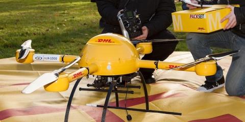 Yellow DHL md4-1000 delivery drone on a tarp while a person holds a DHL Packset box