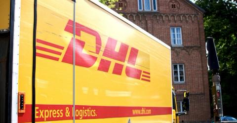 Side of a yellow DHL truck with red logo reading Express & Logistics, parked by a brick building