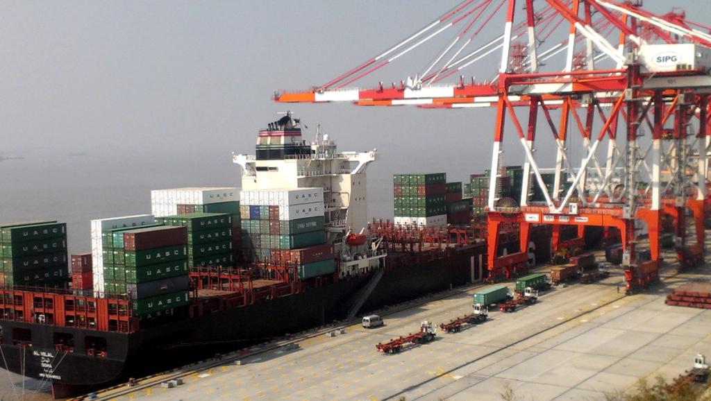 UASC container ship docked beneath red-and-white gantry cranes at SIPG port terminal.