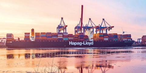 Hapag-Lloyd container ship at a port terminal with cranes at sunset, reflected in calm water