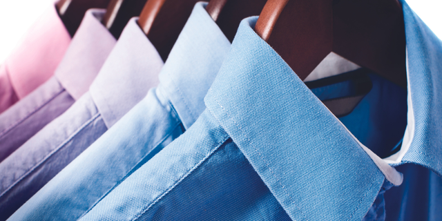Row of pressed blue and lavender dress shirts on hangers with warm light flare, representing fashion airfreight.