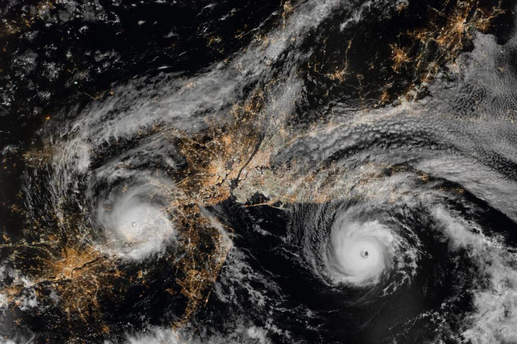Night satellite view of two swirling typhoons over city lights near East Asia