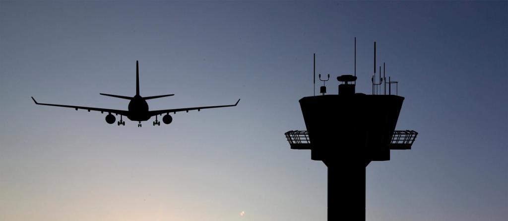 Silhouette of an airliner on approach beside an airport control tower against a dusk sky