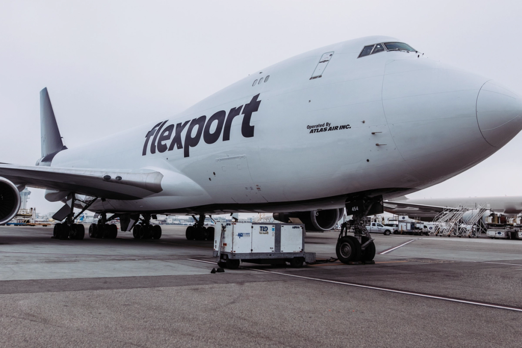 Flexport cargo aircraft parked at an airport with ground support equipment nearby.