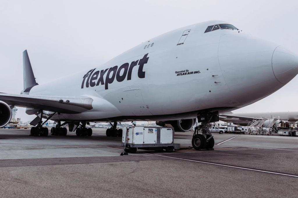 Flexport cargo aircraft parked at an airport with ground support equipment nearby.