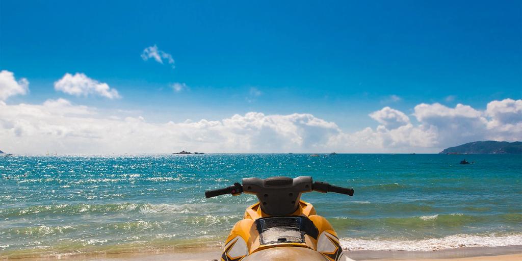 Yellow jet ski parked on a sandy beach facing turquoise sea and a bright blue sky with scattered clouds.