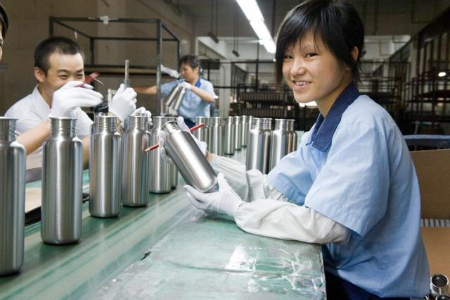 Factory workers in gloves assemble rows of stainless steel water bottles on a production line