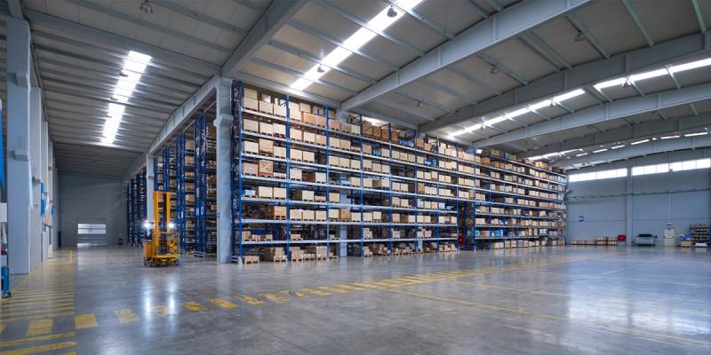 Empty aisle of a large warehouse with tall blue racks of boxed inventory and a yellow forklift.