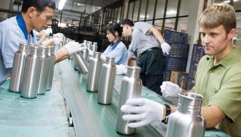 Workers in gloves inspect rows of stainless steel water bottles on a factory assembly line