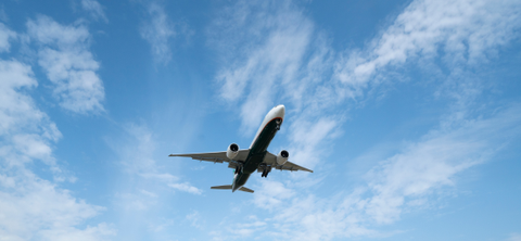 Passenger jet flying low against a bright blue sky with scattered clouds, seen from below