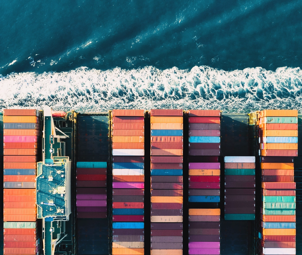 Cargo containers loaded on a ship docked at a beach shoreline with waves.