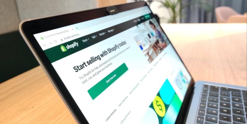 Laptop on a desk showing the Shopify blog page with heading 'Start selling with Shopify today' and a Start free trial button