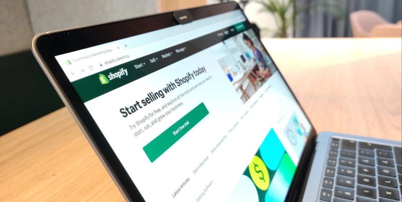 Laptop on a desk showing the Shopify blog page with heading 'Start selling with Shopify today' and a Start free trial button