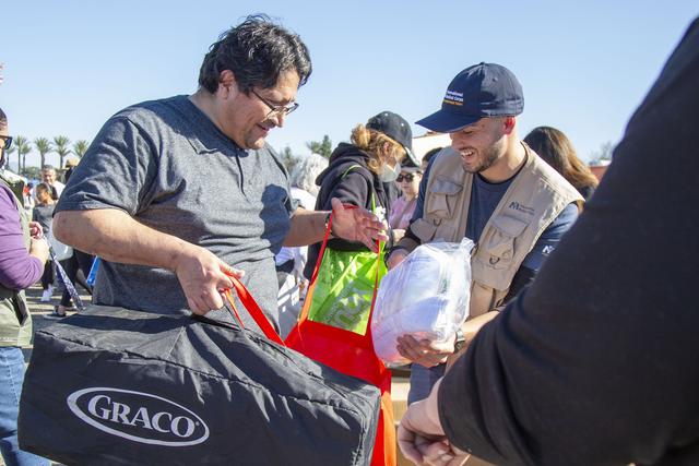 Volunteer in a relief vest handing a baby formula package and Graco bag to a man at an outdoor aid event