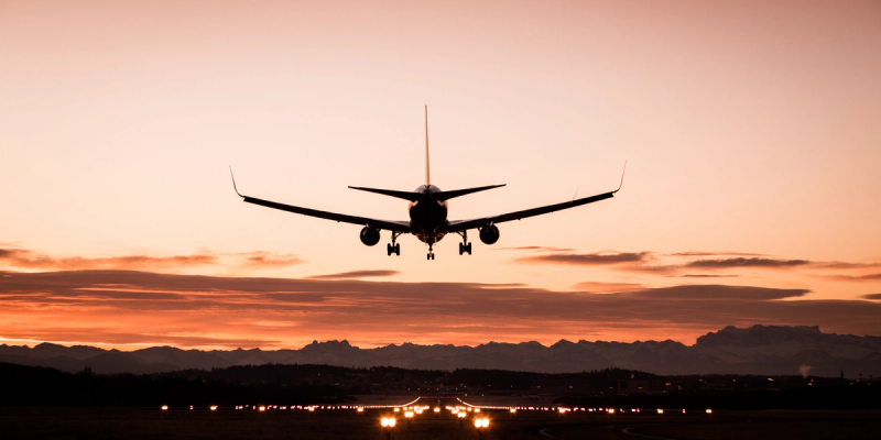 Silhouette of an airplane landing at a runway against an orange sunset sky