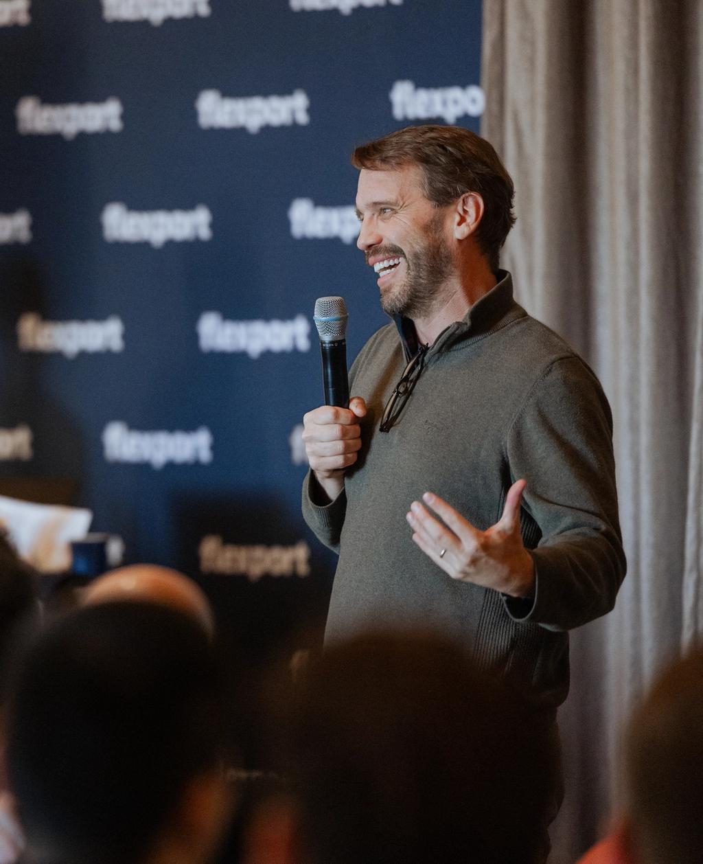 A man speaks into a microphone at a panel discussion while audience members listen.
