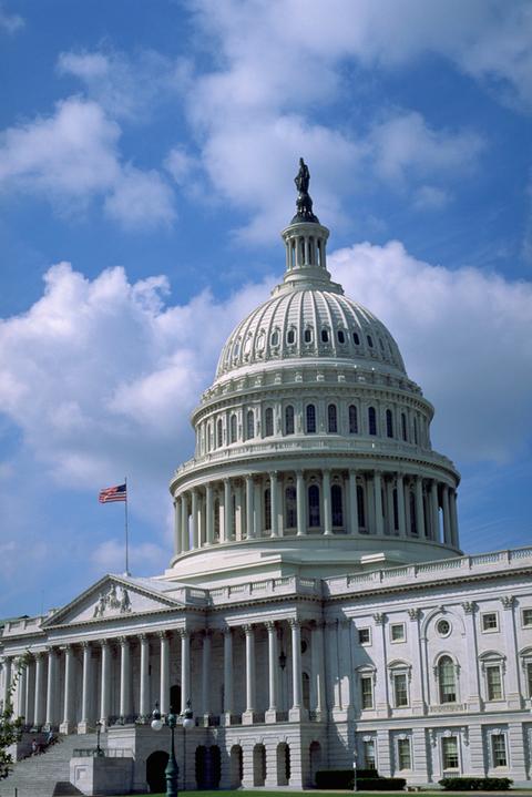 The U.S. Capitol dome with an American flag against a blue sky with clouds