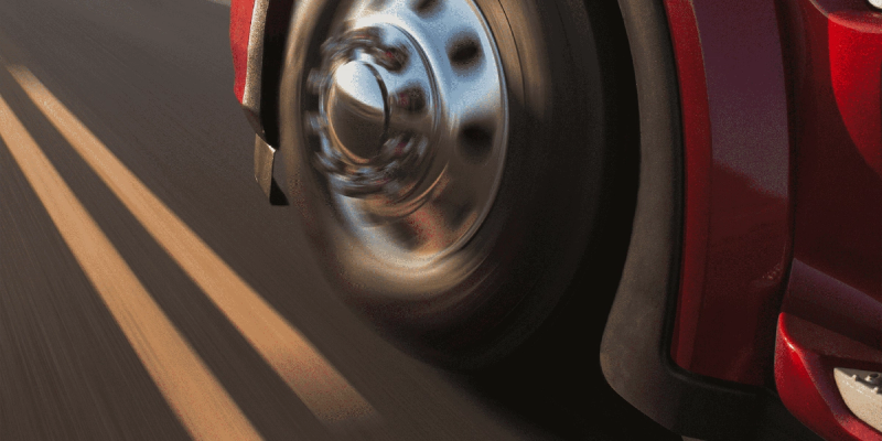 Close-up of a spinning wheel on a moving red truck with motion-blurred road markings