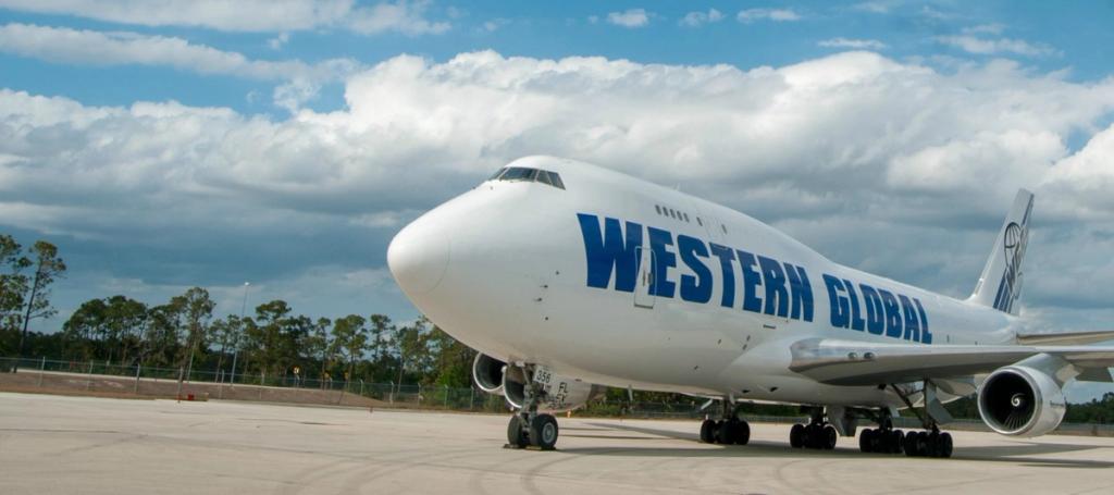 White Western Global Boeing 747 cargo jet parked on an airport tarmac under cloudy sky