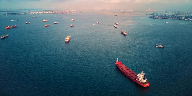 Aerial view of many cargo and tanker ships anchored offshore near a port terminal at dusk