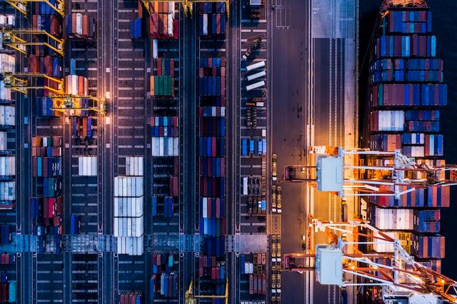 Aerial night view of a container terminal with stacked containers, gantry cranes and lit access roads