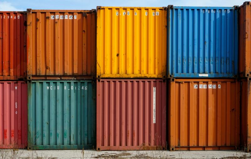 Stacked shipping containers in red, orange, yellow, blue and teal, two rows high, at a depot