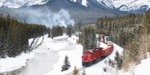 Red freight train hauling containers through a snowy mountain valley of evergreen forest