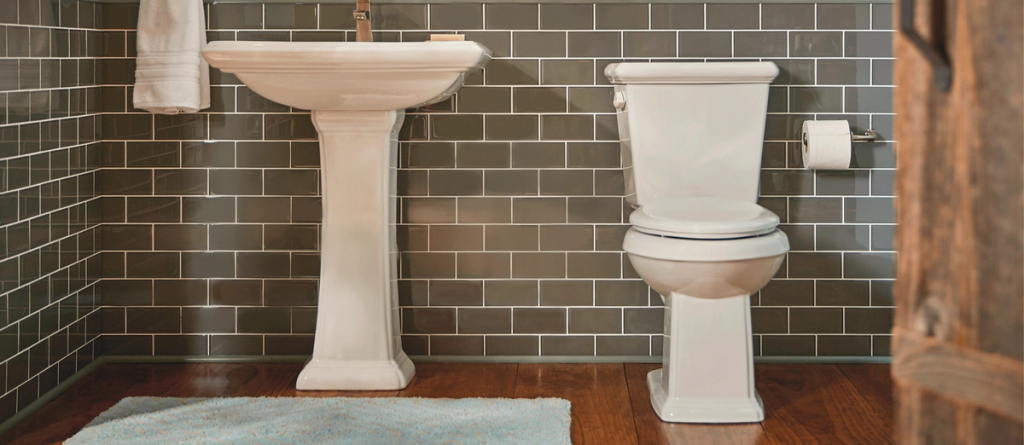 Modern bathroom with white pedestal sink and toilet against gray tile wall and wood floor