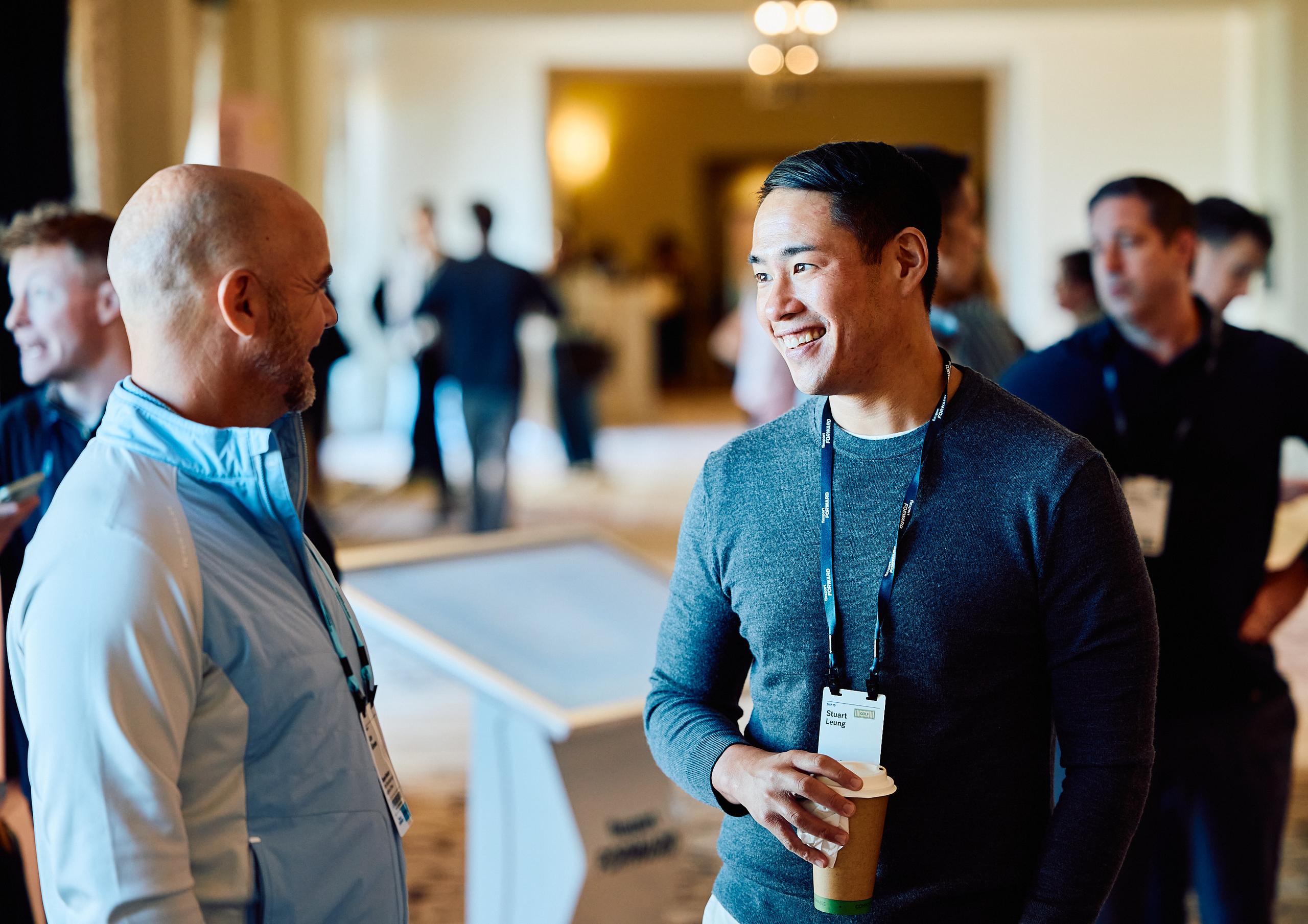 Two professionals wearing gathering badges converse at an indoor event.