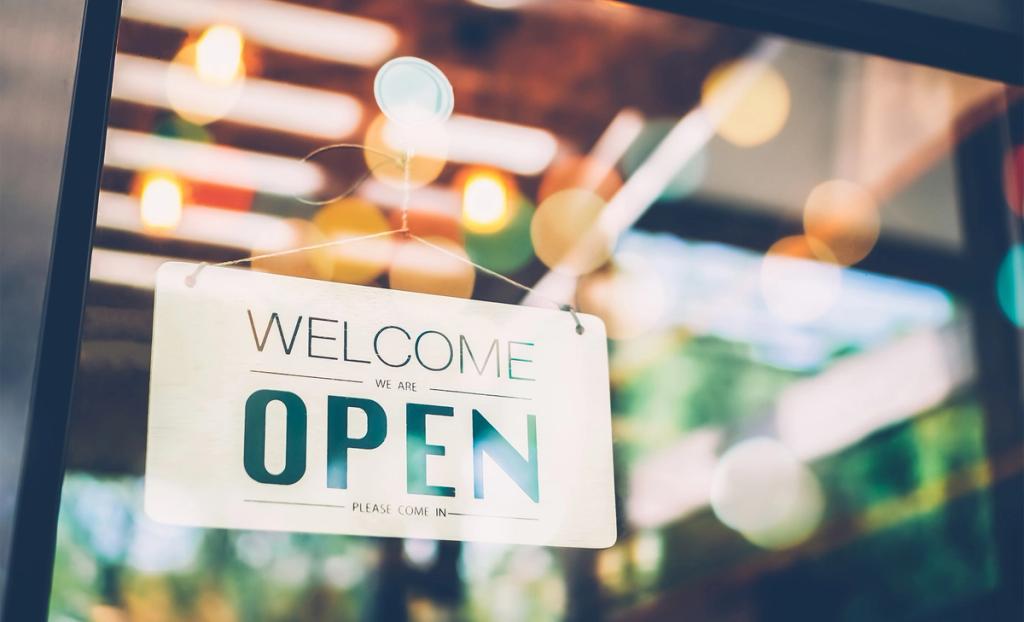 Welcome we are open sign hanging in a shop window with warm bokeh lights behind it