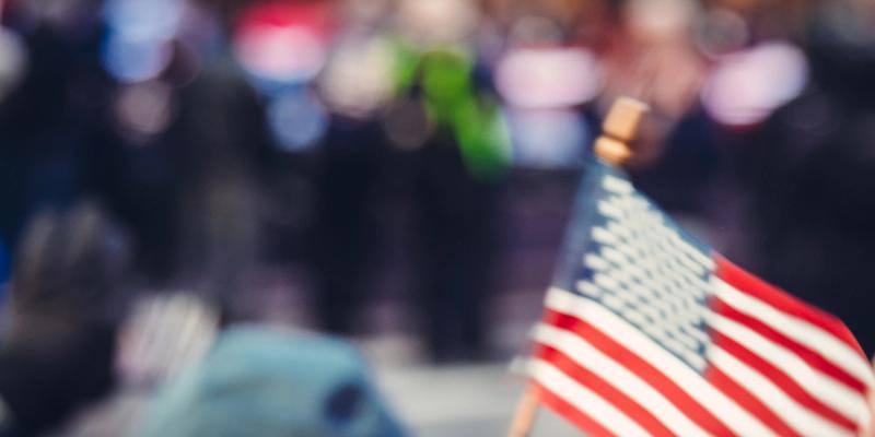 Small American flag held aloft in sharp focus against a blurred crowd of people