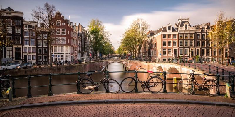 Bicycles leaning on a bridge railing over an Amsterdam canal lined with Dutch row houses