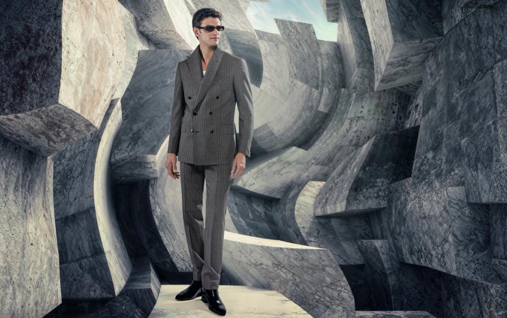 Man in a gray pinstripe double-breasted suit posing inside a gray stone sculptural set
