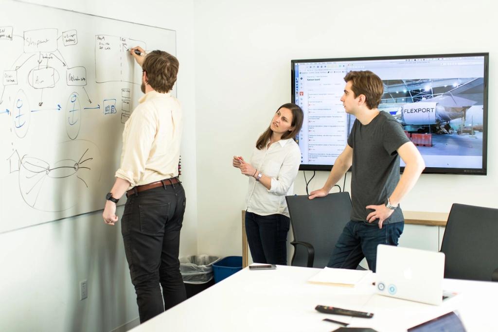 Three coworkers in an office, one diagramming a shipment flow on a whiteboard, a Flexport screen behind them